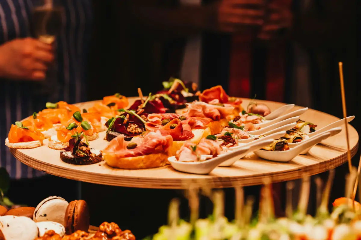Assorted gourmet hors d'oeuvres, including prosciutto crostini and smoked salmon appetizers, served on a wooden platter at a professional event.